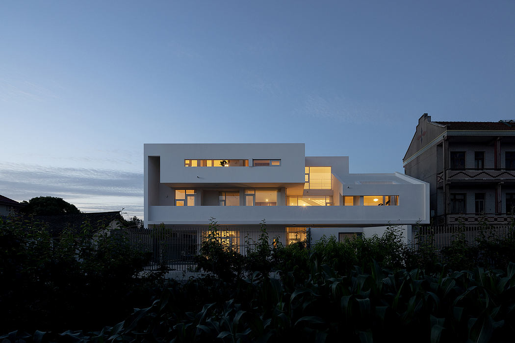 A modern, minimalist residential building with large windows and a warm, ambient lighting.