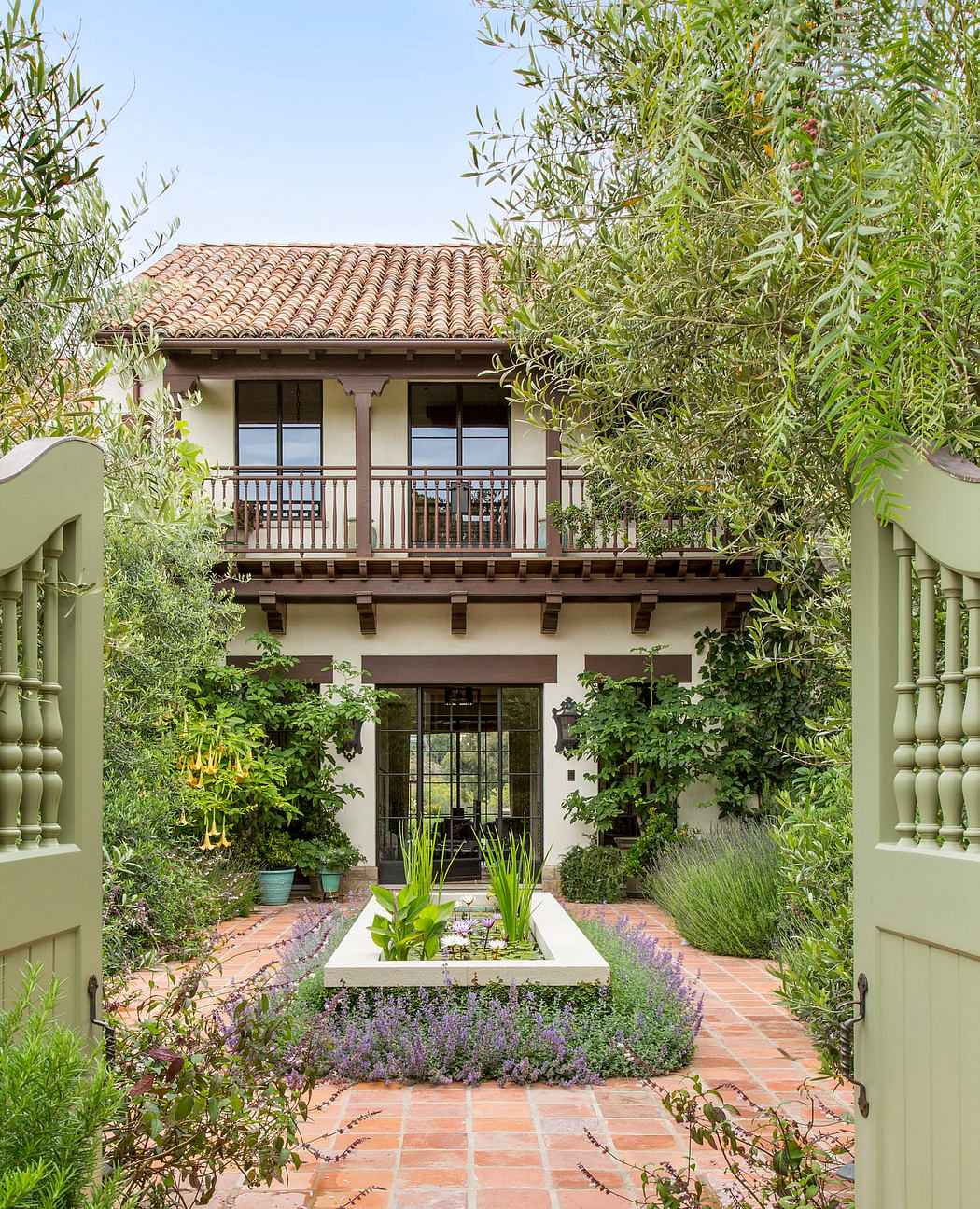 A verdant, Spanish-style courtyard with terracotta tile roof, wooden beams, and lush vegetation.