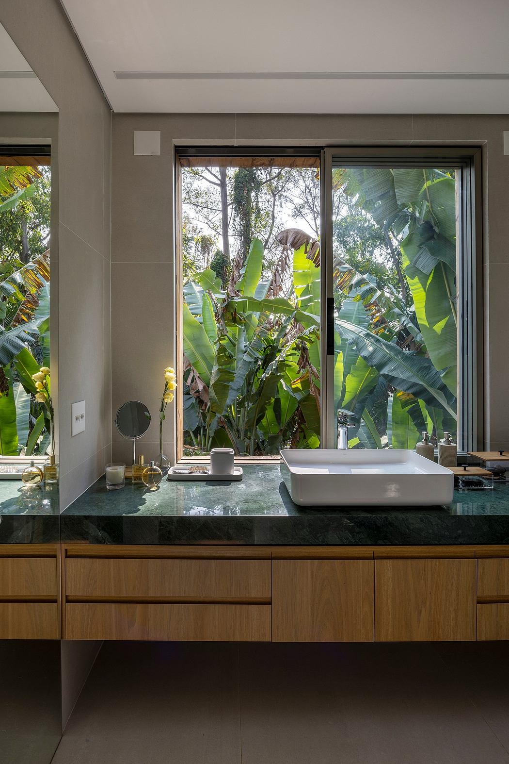 Spacious bathroom with floor-to-ceiling windows overlooking lush greenery, sleek vanity, and modern fixtures.