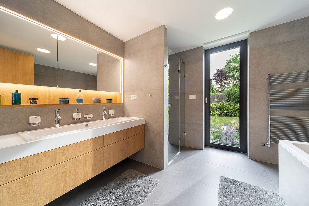 A modern bathroom with a large vanity, recessed lighting, and a view of the lush greenery outside.