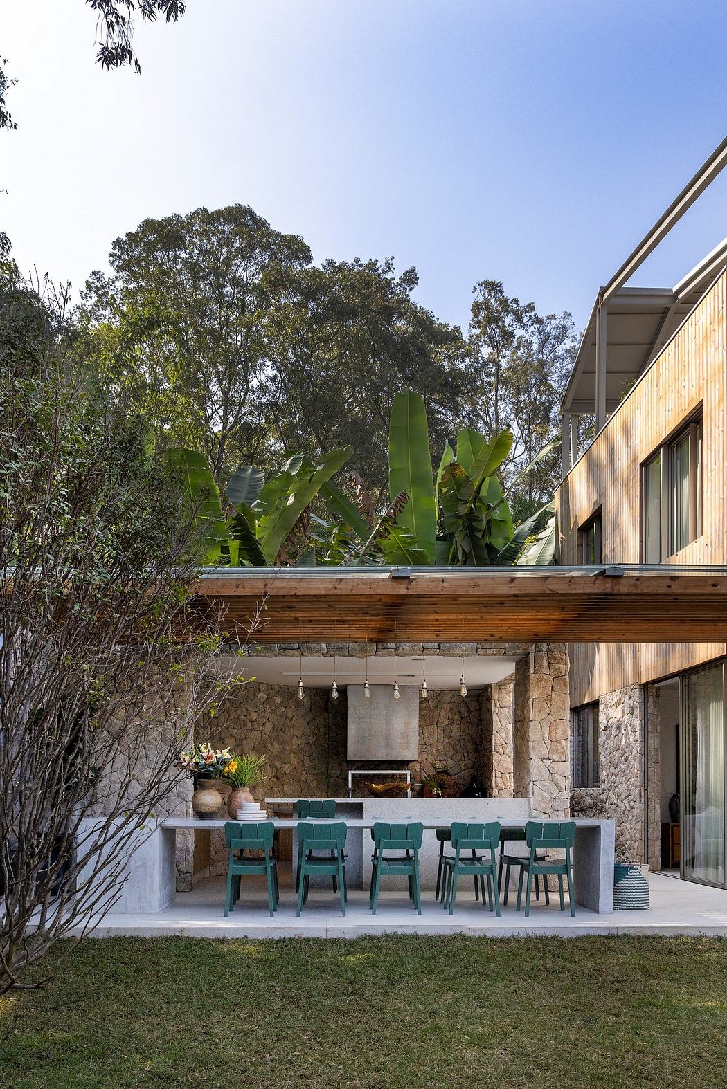 Rustic outdoor living space with wooden deck, stone walls, and vibrant tropical foliage.