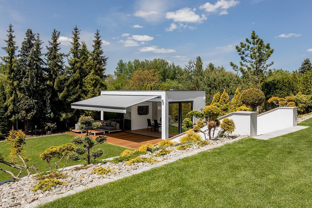 Modern, single-story home with covered patio, surrounded by lush gardens and mature trees.
