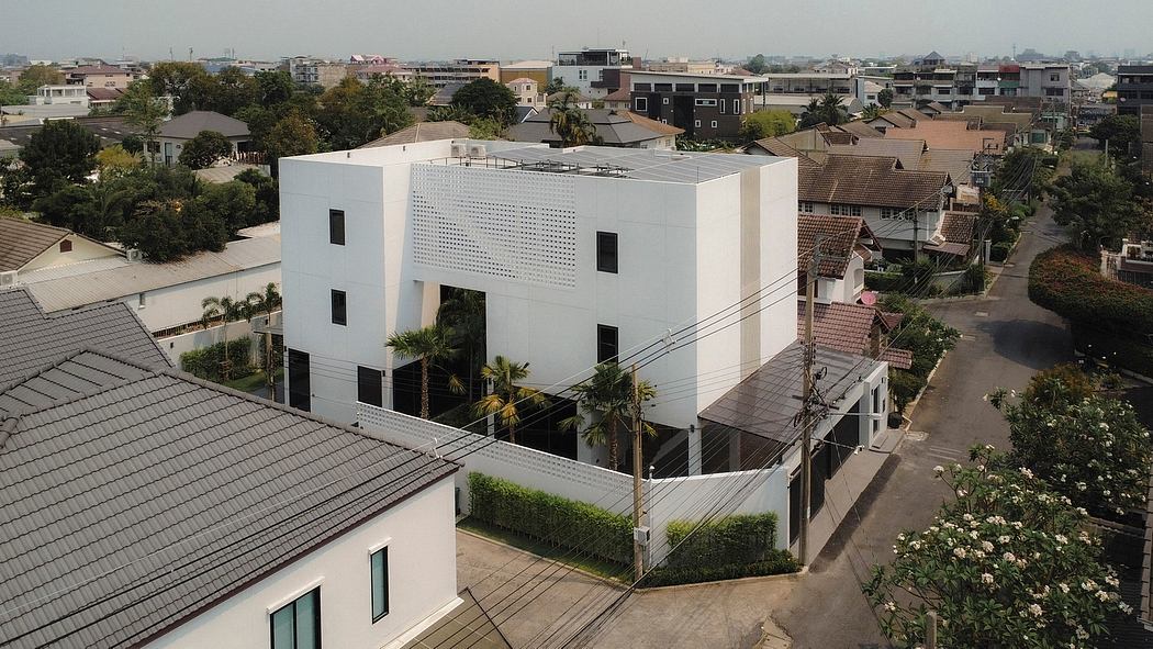 Large, modern white building with perforated exterior, surrounded by trees and smaller structures.
