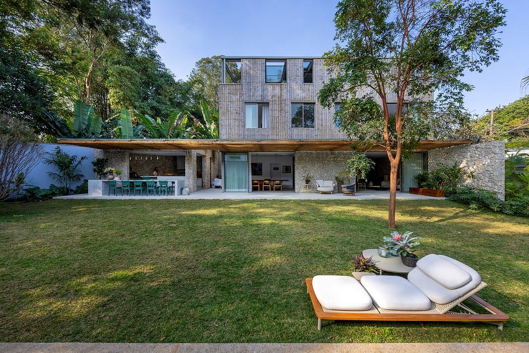 A modern, wooden-clad home with a covered terrace, surrounded by lush greenery and a well-manicured lawn.