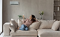 Smiling woman using air conditioner remote controller, relaxing on couch